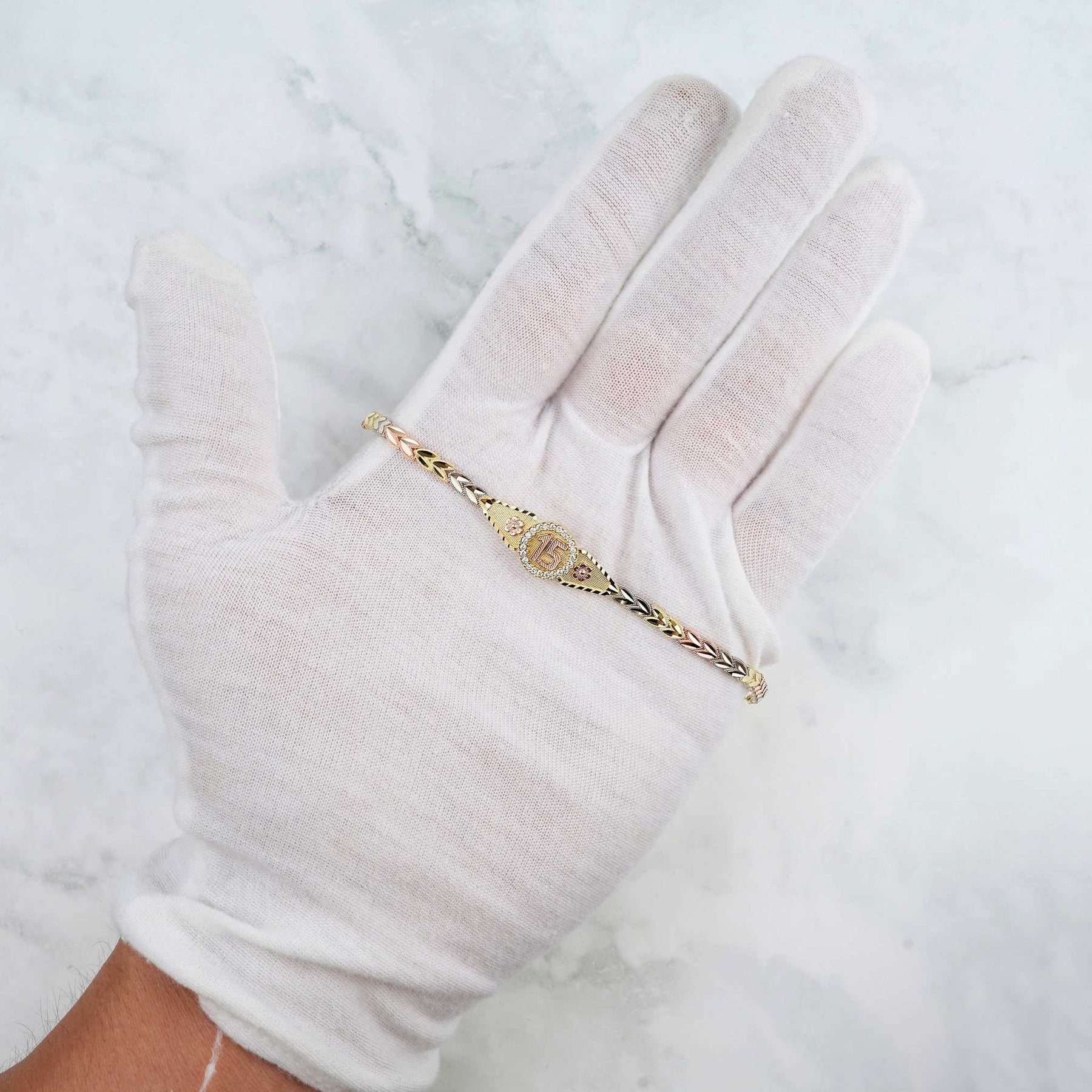 Close-up of the tri-color gold Quinceañera leaf bracelet showcased on a gloved hand.