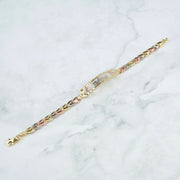 A tricolor yellow gold and rose gold charm bracelet with a central pavé diamond band, displayed diagonally on a white marble background.