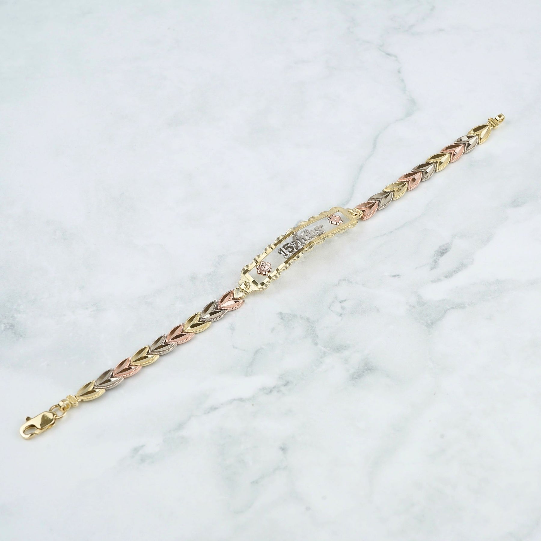 A tricolor yellow gold and rose gold charm bracelet with a central pavé diamond band, displayed diagonally on a white marble background.