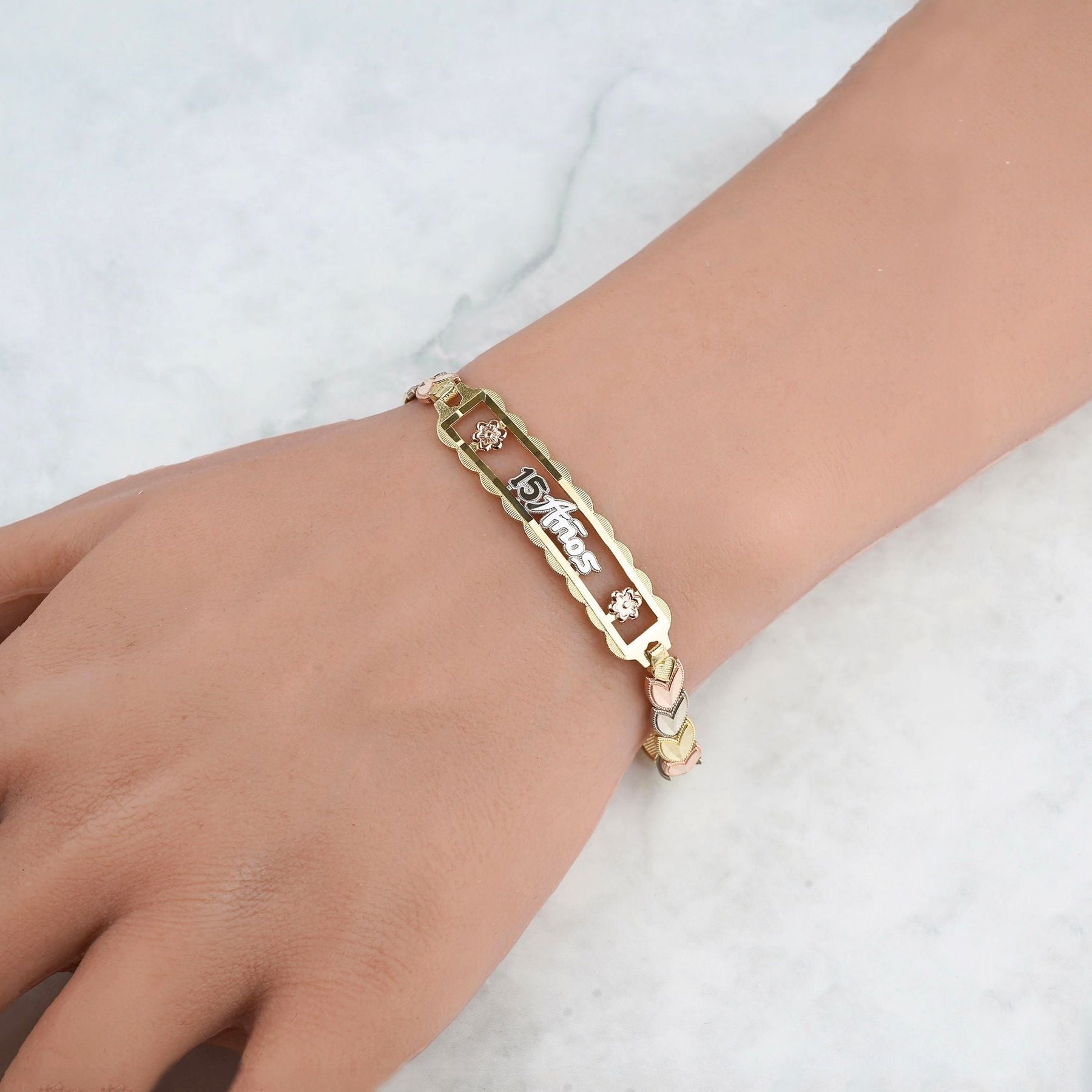 Tricolor gold "15 Años" leaf charm bracelet worn on a bare wrist.