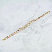 A three-tone chain bracelet with alternating yellow gold, rose gold, and silver-toned links, displayed diagonally on a white marble background.