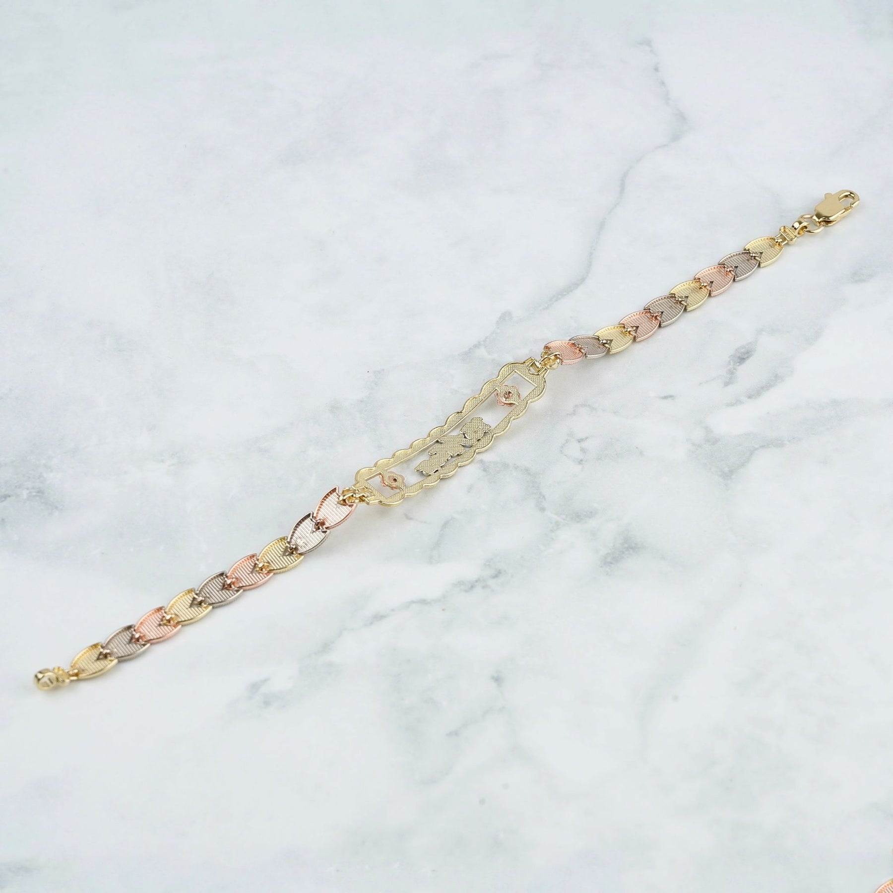 A three-tone chain bracelet with alternating yellow gold, rose gold, and silver-toned links, displayed diagonally on a white marble background.
