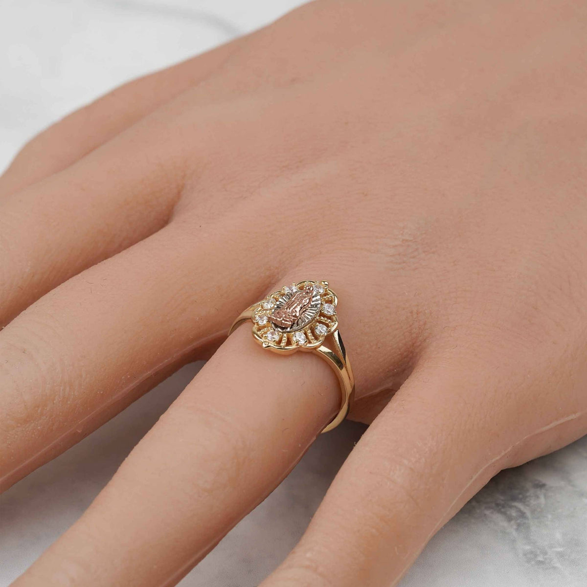 Detailed angled shot of the tricolor gold Virgin Mary ring worn on a hand.