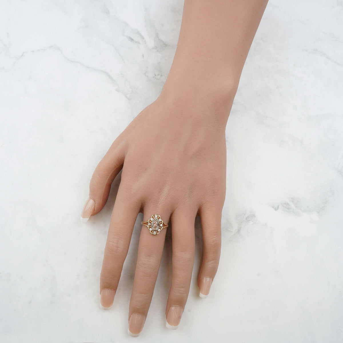 Hand wearing the polished tricolor gold Virgin Mary ring against a marble background.