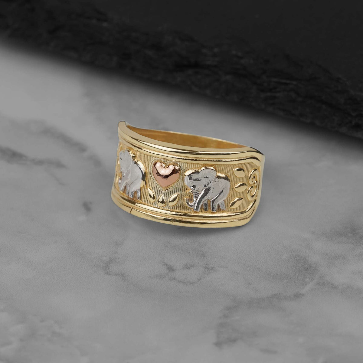 Tri-color gold elephant ring featuring detailed engravings resting on a marble surface.