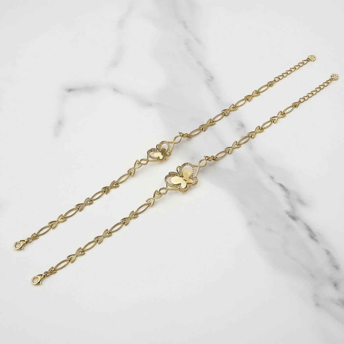 Two gold two-tone Virgin Mary Guadalupe butterfly bracelets laid diagonally on white marble