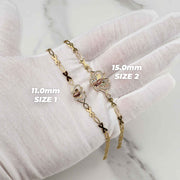 Gloved hand holding two gold Virgin Mary butterfly bracelets labeled 11.0mm Size 1 and 15.0mm Size 2.