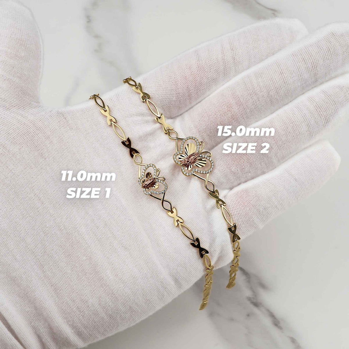 Gloved hand holding two gold Virgin Mary butterfly bracelets labeled 11.0mm Size 1 and 15.0mm Size 2.