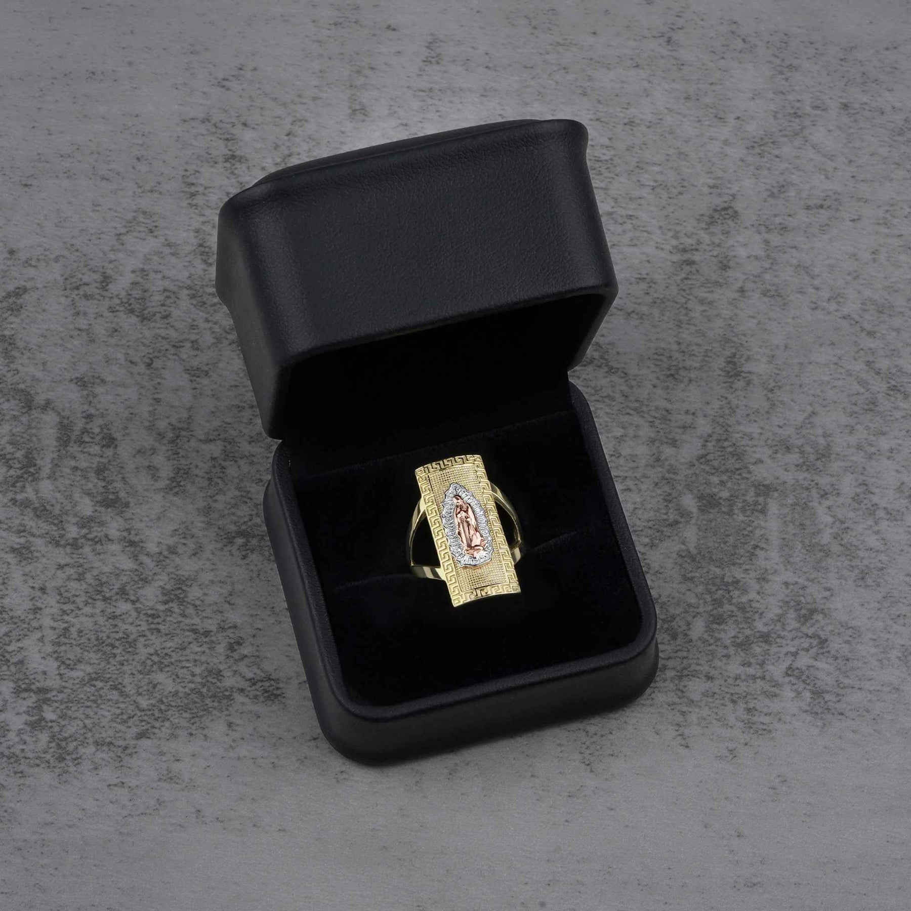 10k - 14k gold ring with a Virgin Mary design in a black jewelry box on a gray surface