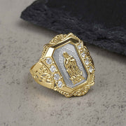 Gold and white gold Virgin Mary Guadalupe ring with cubic zirconia on textured background.