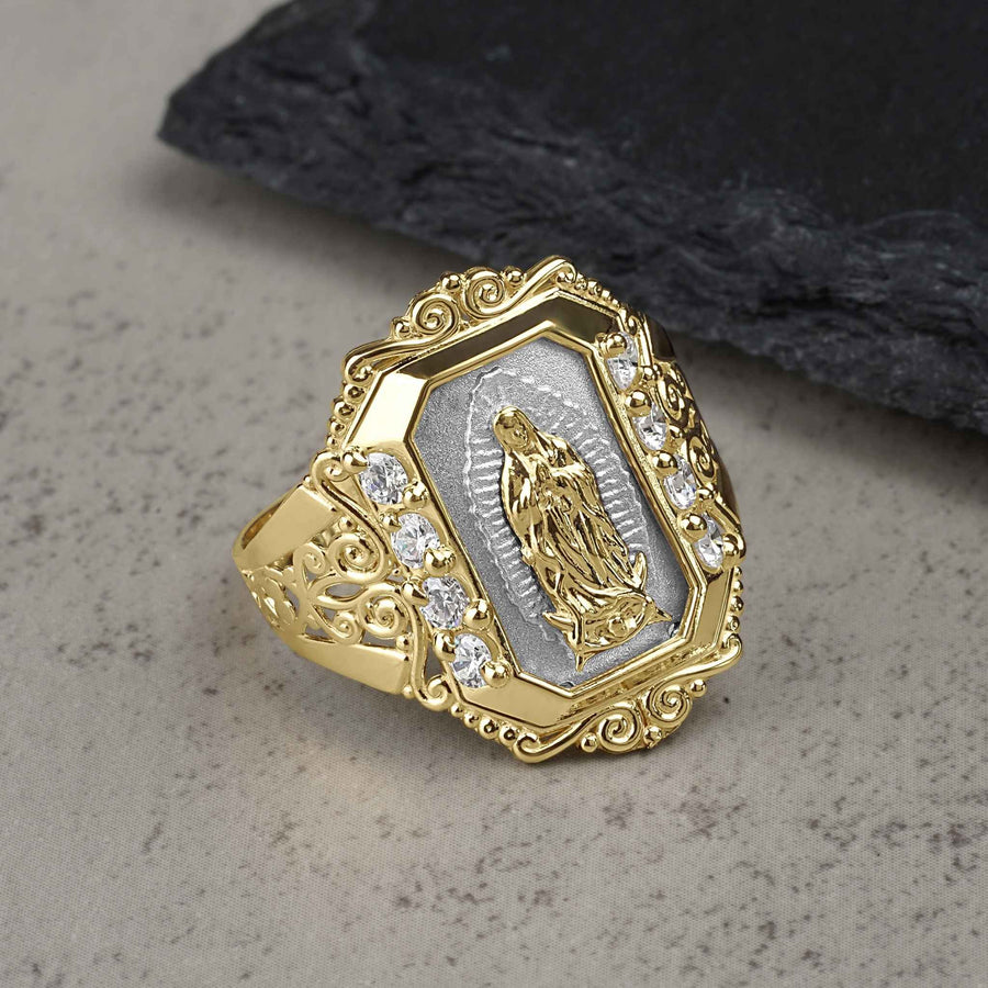 Gold and white gold Virgin Mary Guadalupe ring with cubic zirconia on textured background.