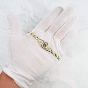 Tri-color gold quinceañera bracelet featuring a central "15" medallion, displayed on a white-gloved hand.