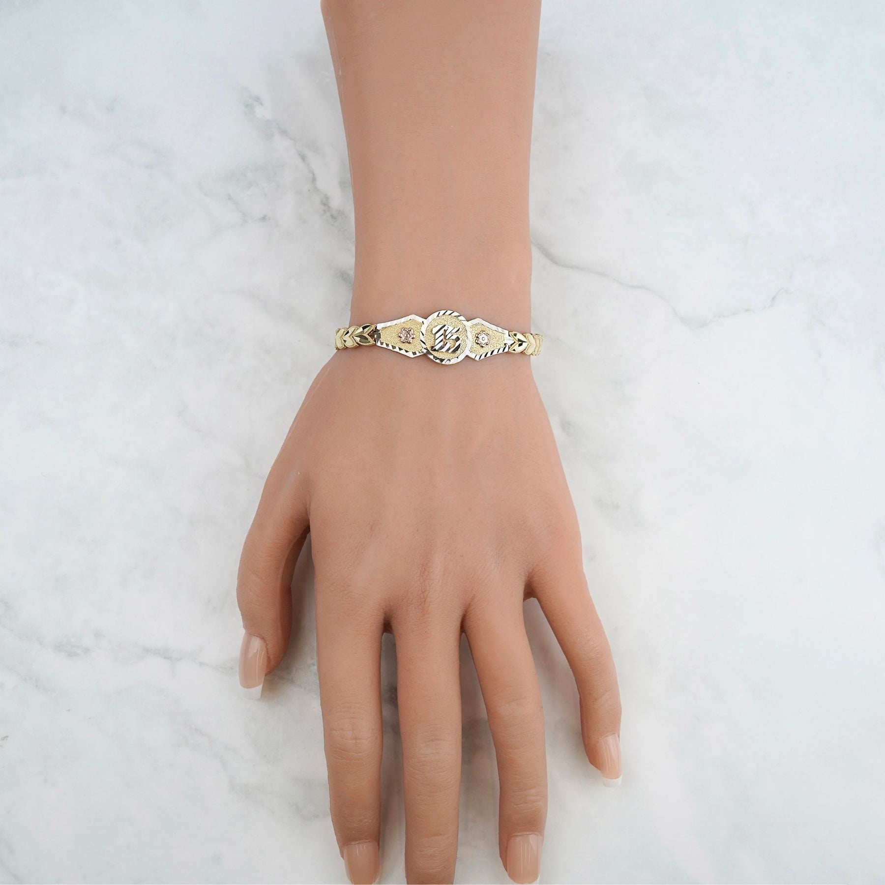 Elegant shot of the 10k & 14k gold "15 Anos" celebratory bracelet displayed on a marble surface.