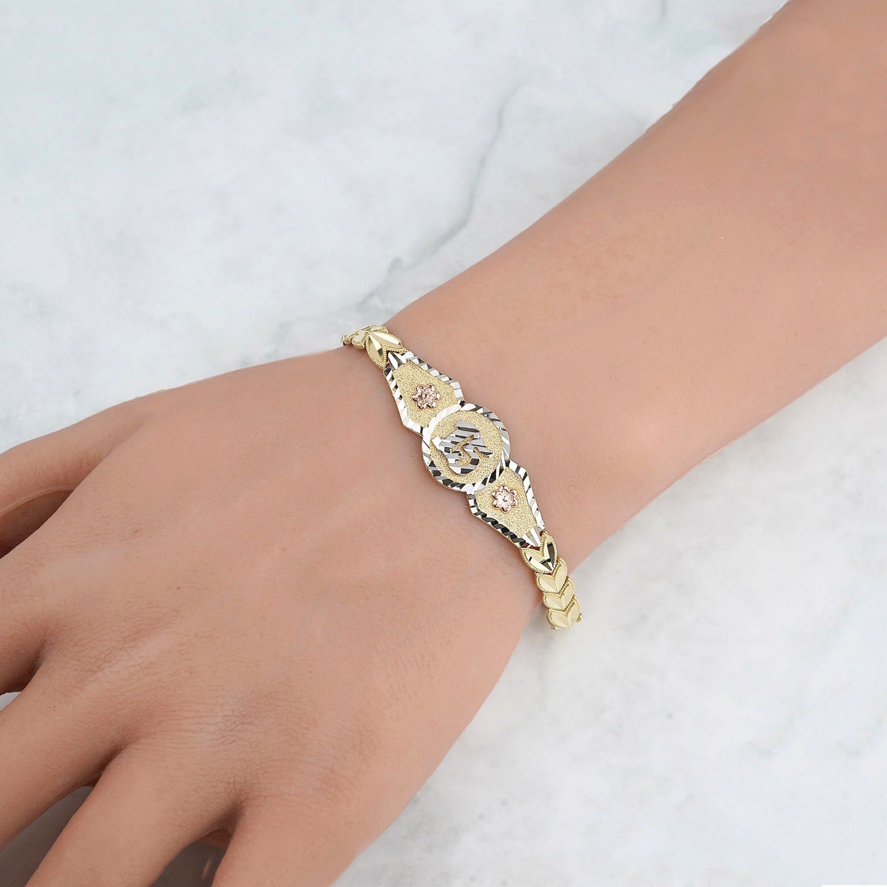 Close-up of the tri-color gold quinceañera leaf bracelet showing the central "15" medallion.