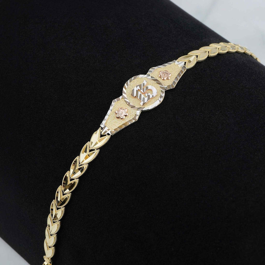 Detail view of a gold "15 Años" leaf link bracelet on dark display background.