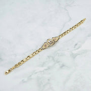 Tri-color gold "15 Años" leaf link bracelet laid diagonally on a marble background.