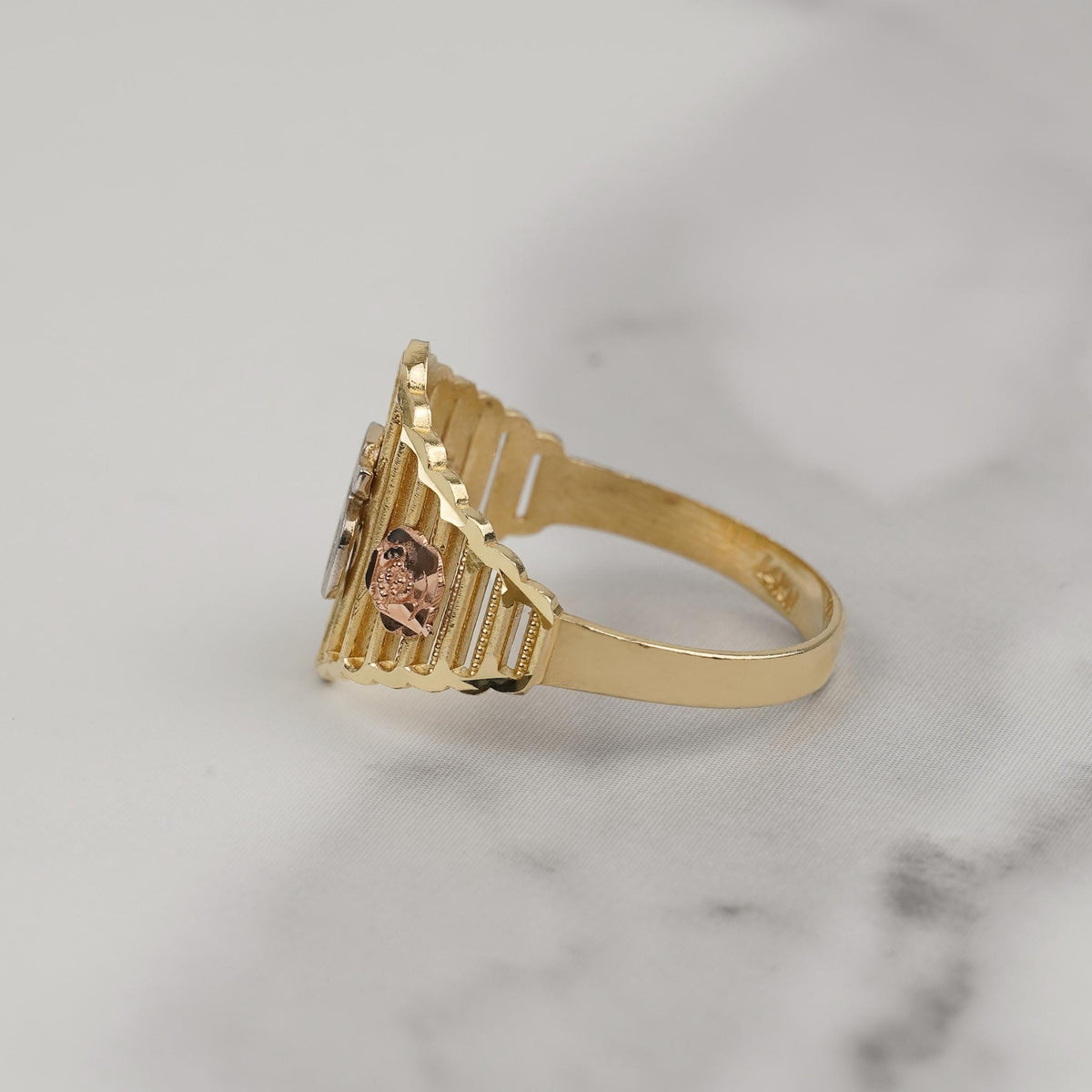 Side view of a tricolor gold Quinceañera ring on marble surface.