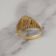 Back view of a gold Quinceañera ring with a slotted cutout face on marble.