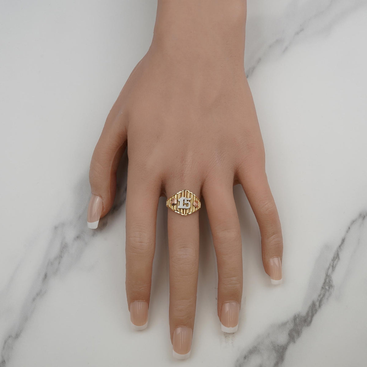 Tricolor gold Quinceañera ring with number 15 worn on a hand against marble.