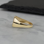 Side view of a polished gold round signet ring on marble background.