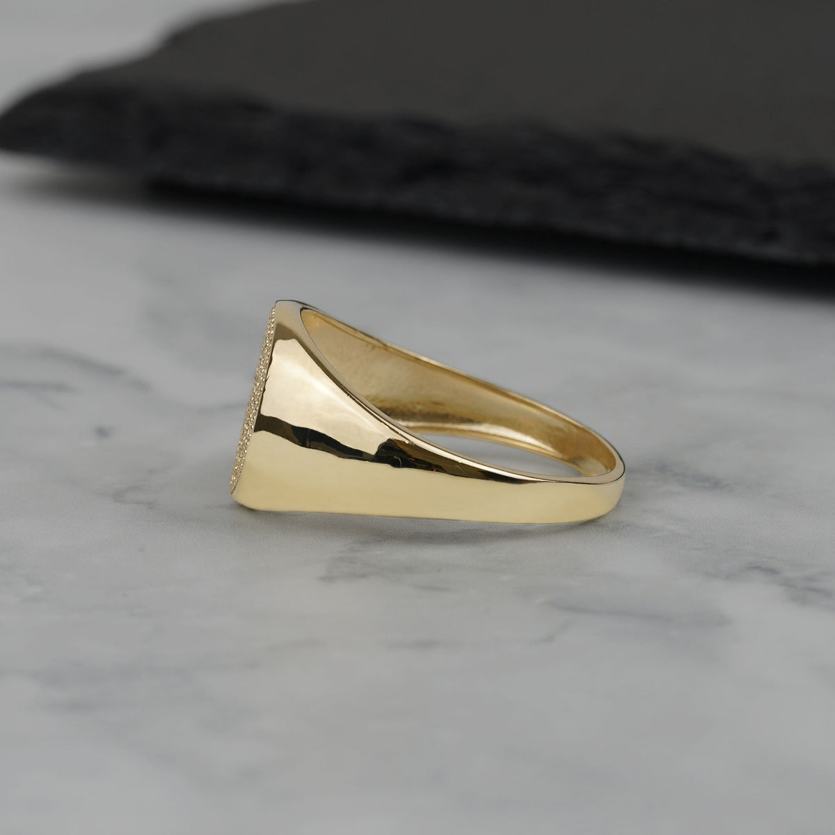 Side view of a polished gold round signet ring on marble background.