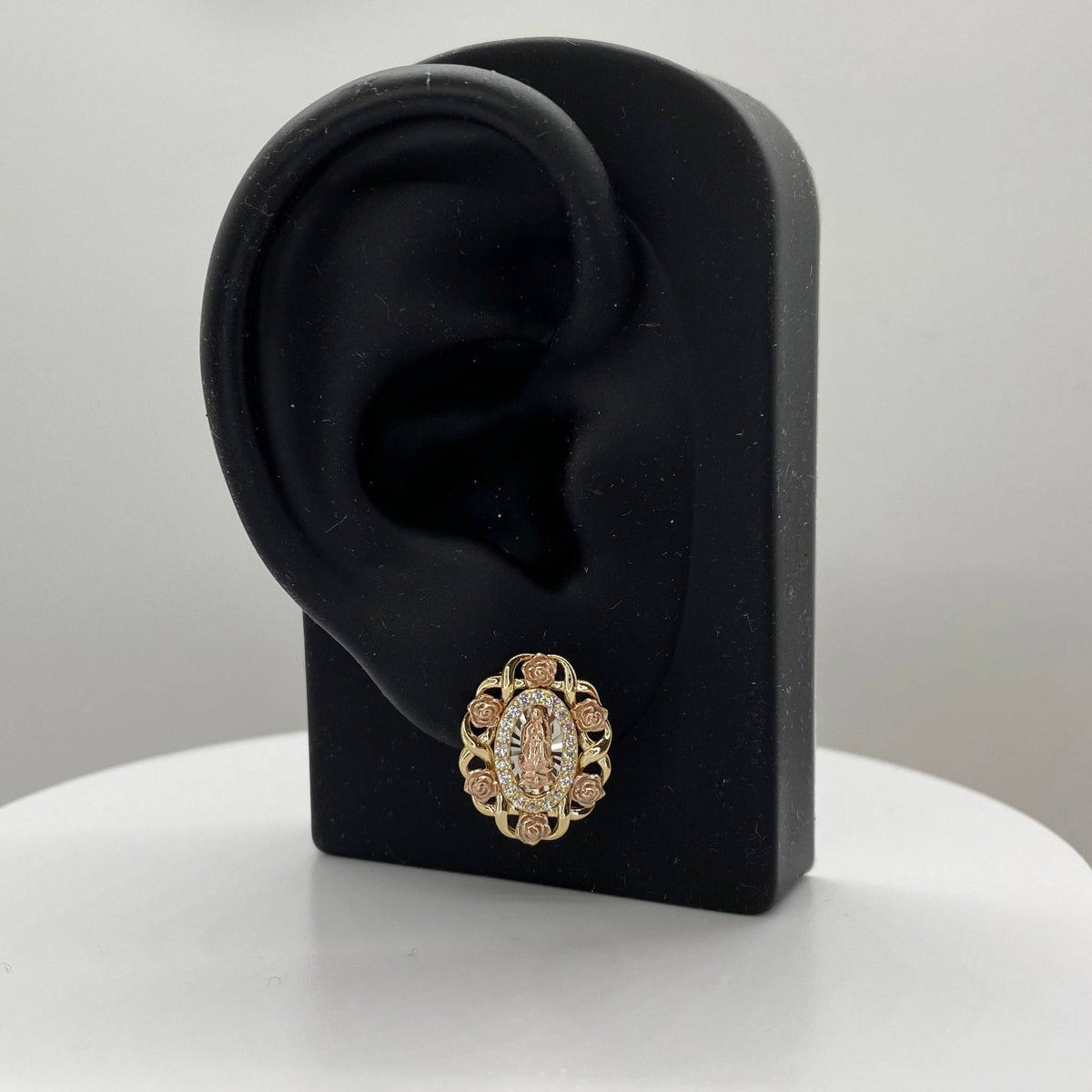 Tri-color gold Virgin Mary oval stud earring displayed on a black ear-shaped jewelry stand.