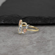 Side-profile view of a gold tri-color Virgin Mary heart ring on a stone surface.