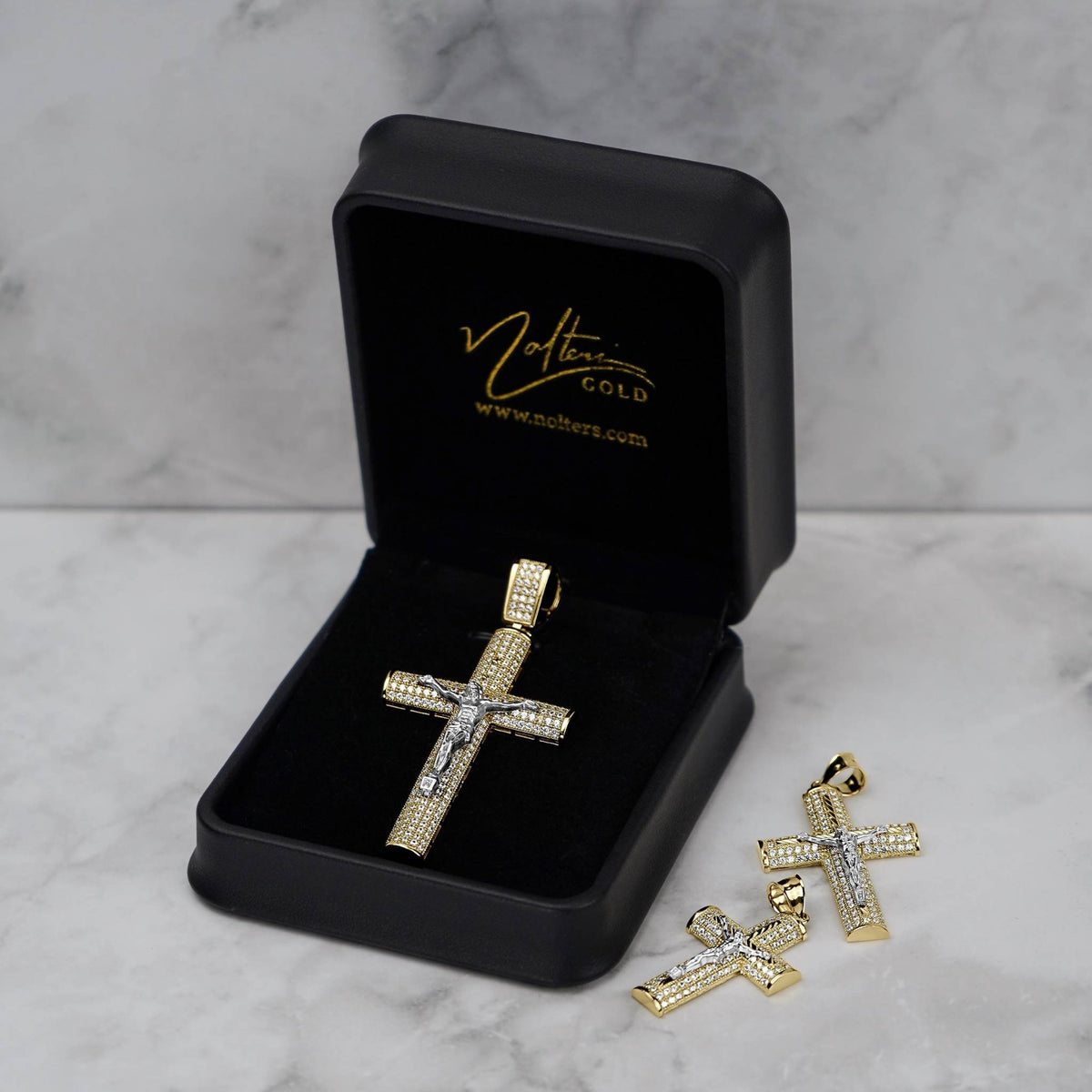 Gold Hermo iced crucifix pendant in black Nolters jewelry box next to two additional pendants