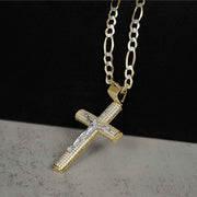 Angled view of two-tone gold Hermo iced crucifix pendant on a pave Figaro chain resting on a dark stone surface.