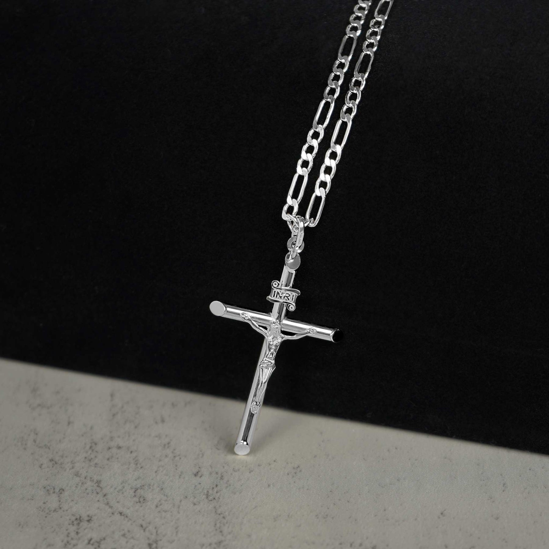 White gold tubular INRI crucifix necklace on a chain against a two-tone background.