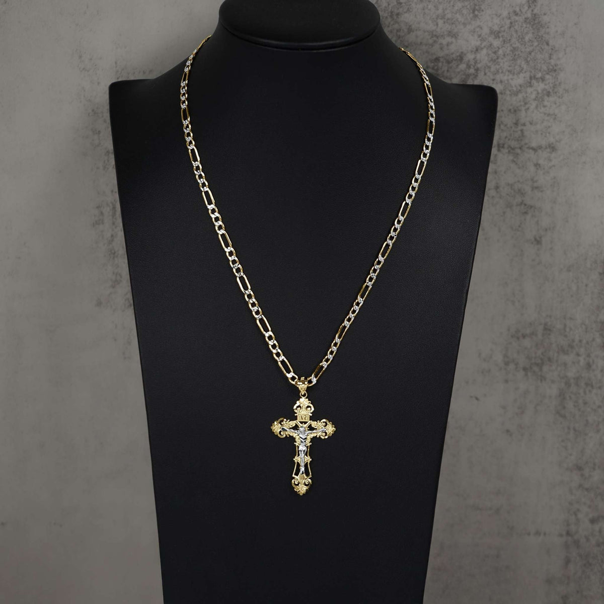 Two-tone gold INRI crucifix pendant necklace on Figaro chain displayed on black display bust.