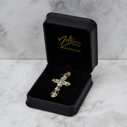 Ornate gold cross pendant displayed in a black velvet-lined jewelry box on a marble surface.