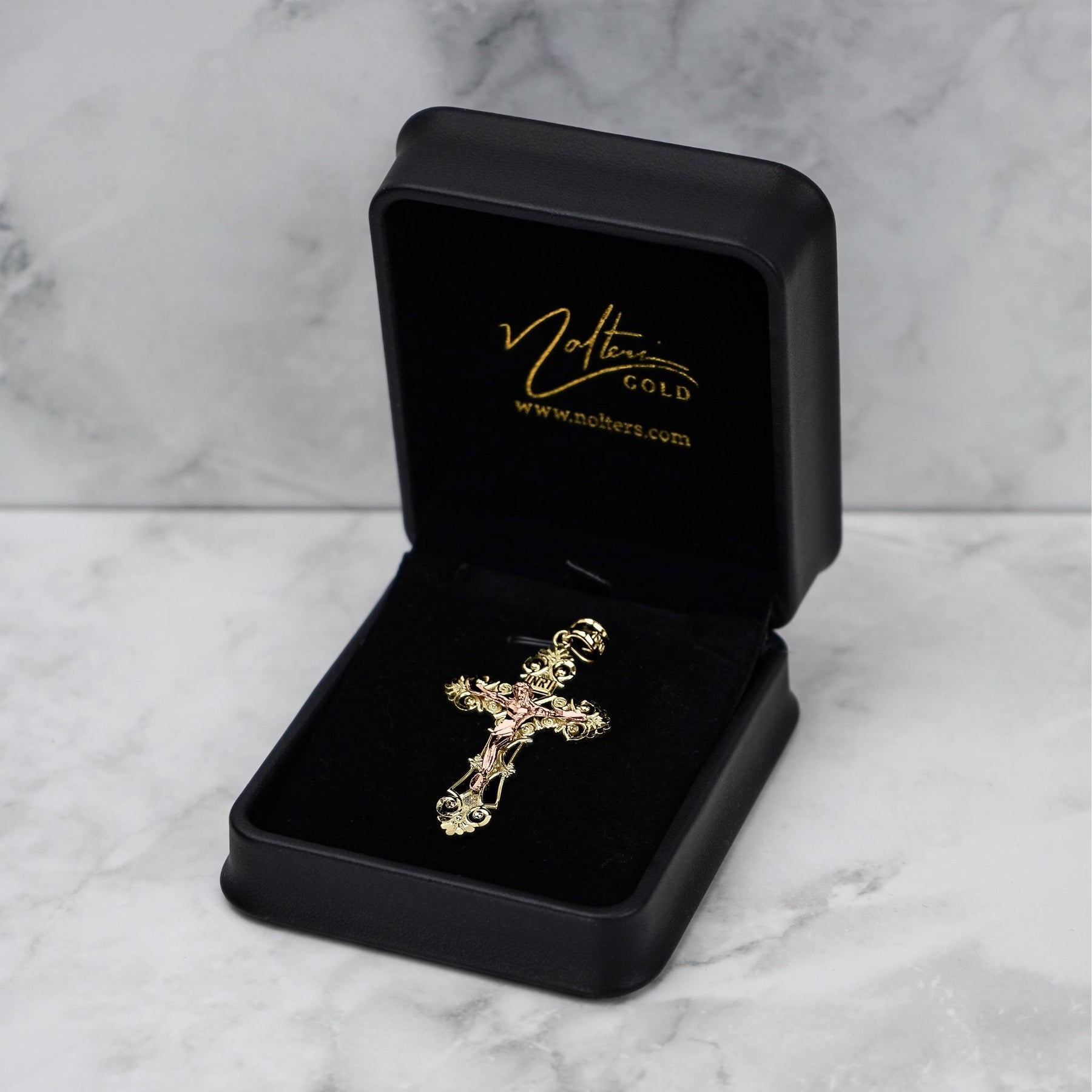 Two-tone gold crucifix pendant displayed inside an open black Nolters branded gift box.