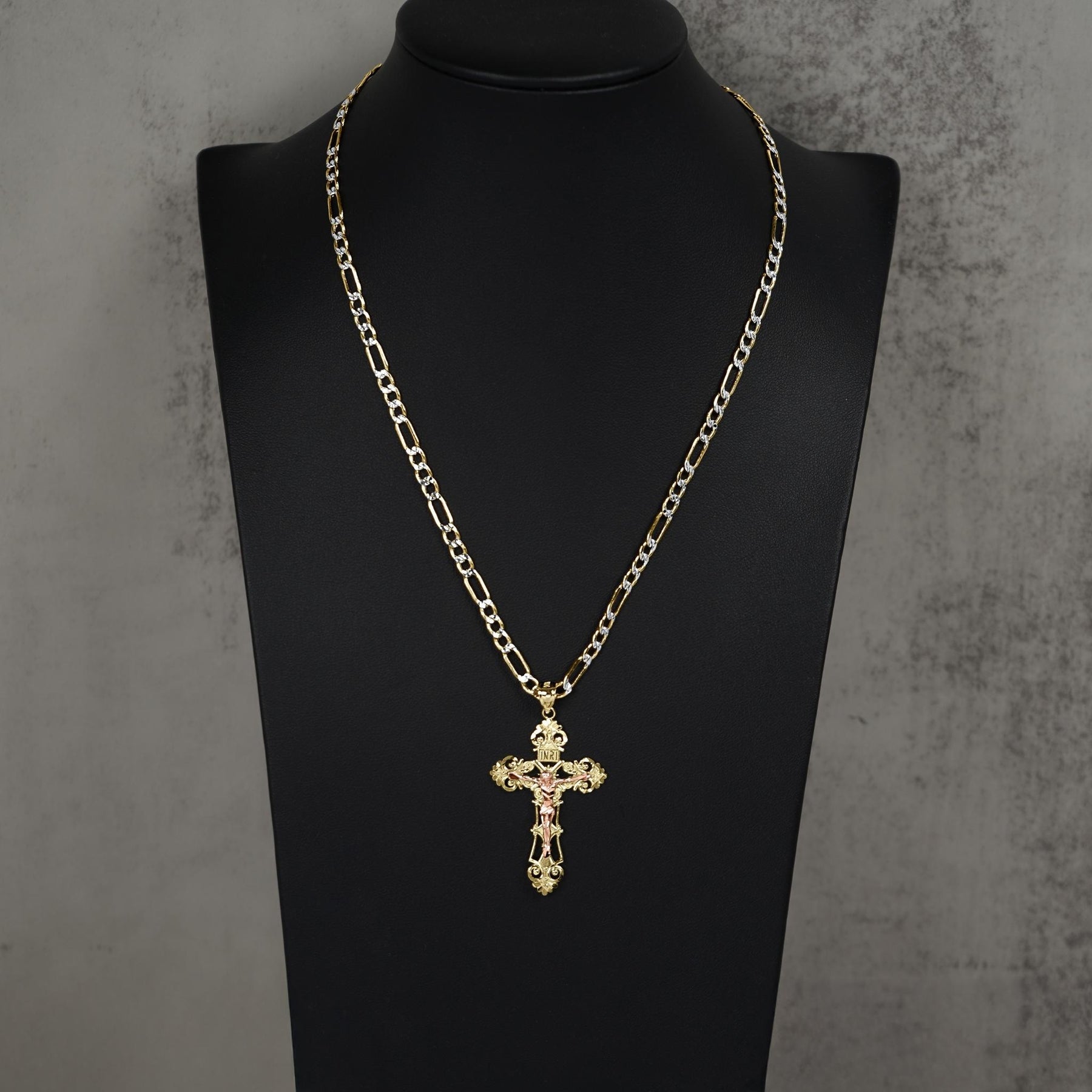 A gold chain necklace with a cross pendant displayed on a black mannequin bust against a textured gray background.
