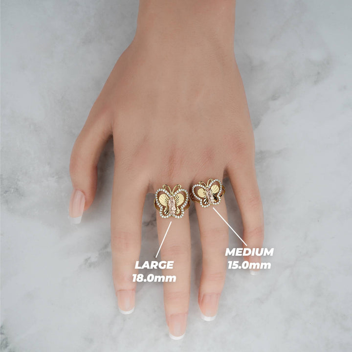 Large and medium gold butterfly rings on a hand over a marble background.