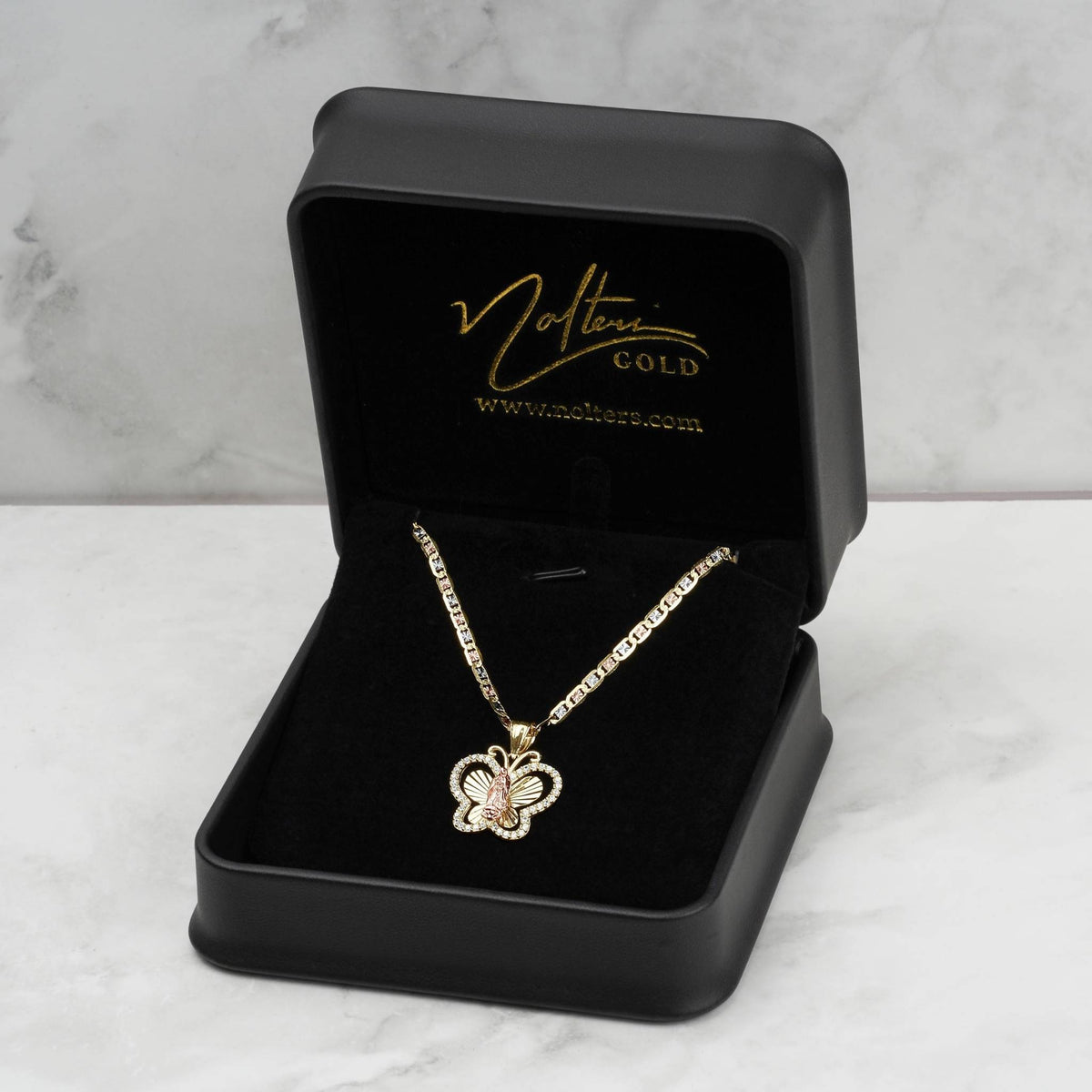 Gold Virgin Mary Guadalupe butterfly CZ pendant necklace displayed inside an open black jewelry box on marble.