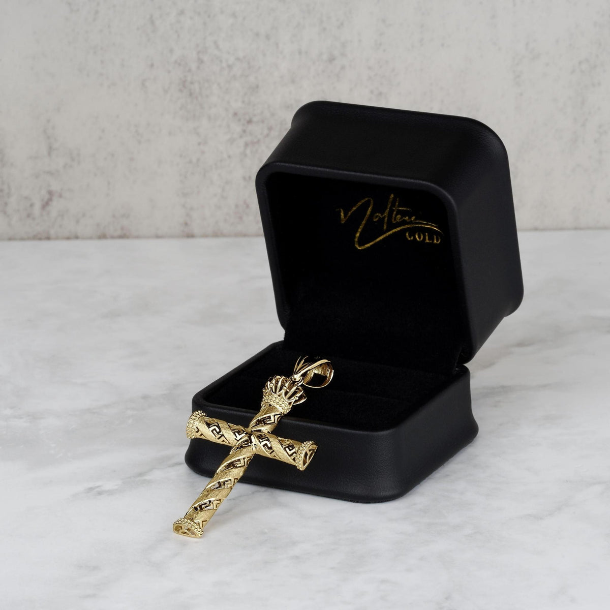 Gold crowned cross pendant resting next to an open black leather jewelry box.