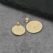Two gold-toned round pendant charms with bail loops, featuring engraved lettering on a textured gray surface.