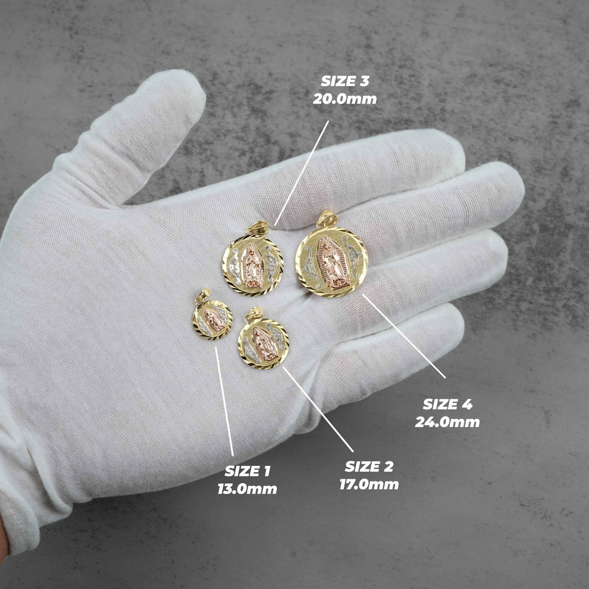 White-gloved hand holding four oval tri-color gold Virgin Mary pendants in ascending size order from 13.0mm to 24.0mm.