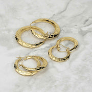 Assortment of textured gold rhombus hoop earrings displayed on a marble surface.