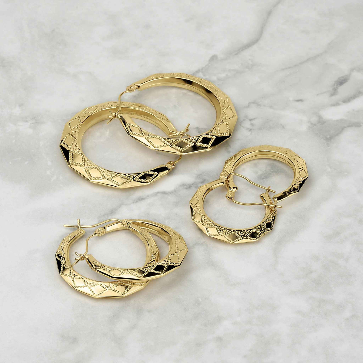 Assortment of textured gold rhombus hoop earrings displayed on a marble surface.