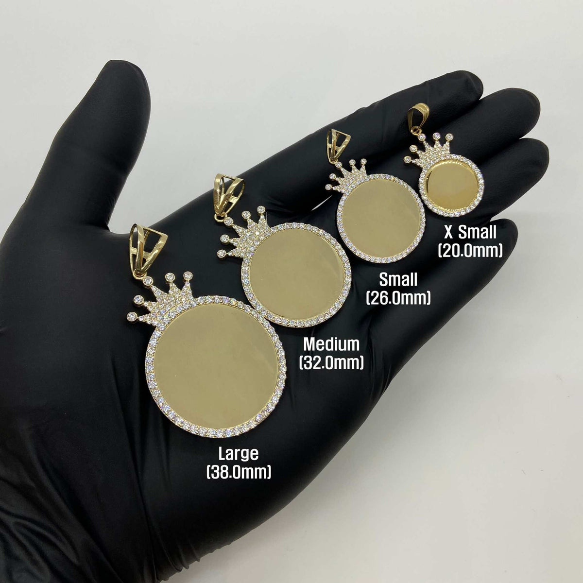 Four gold crown picture pendants in varying sizes displayed in a hand for scale comparison.