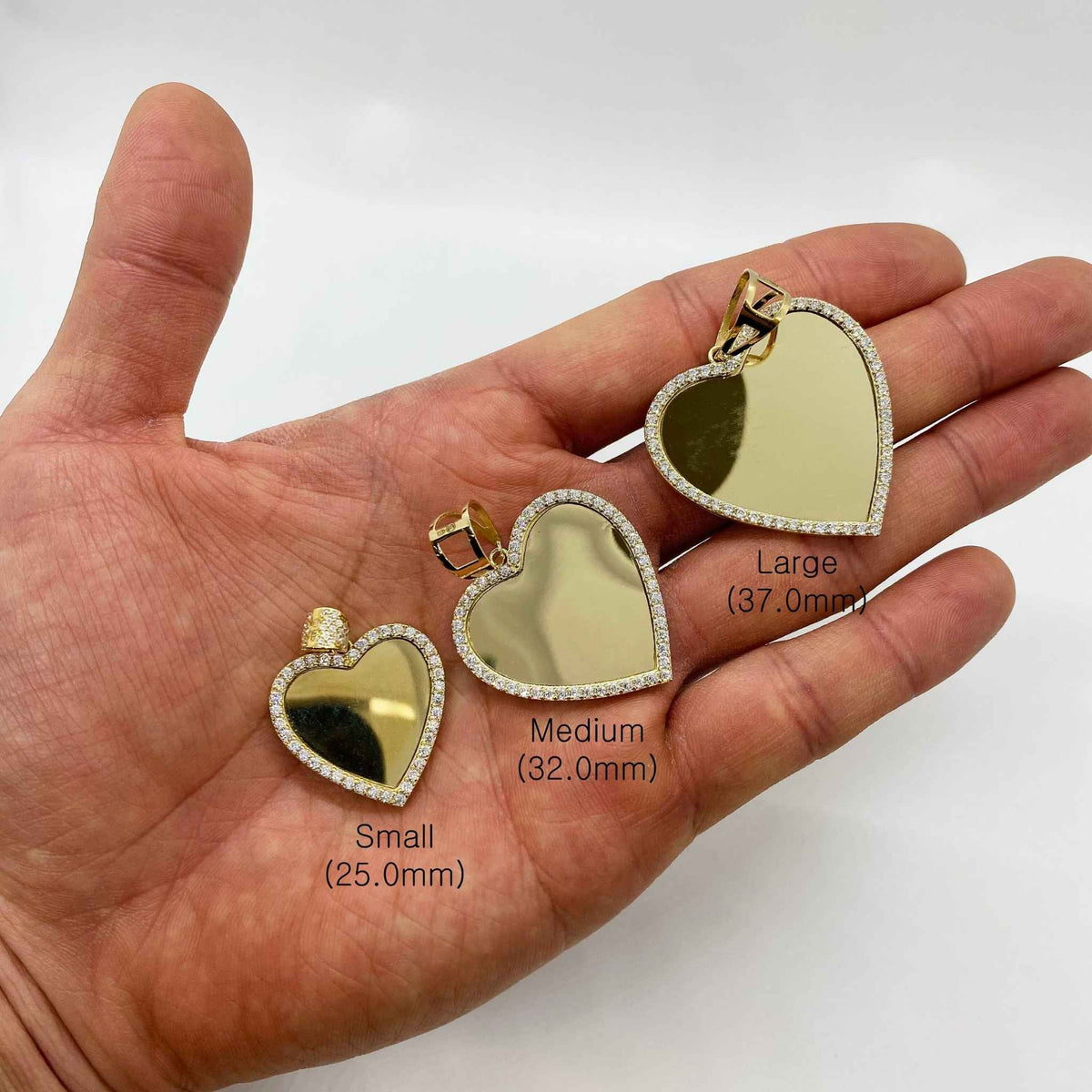Small, Medium, and Large gold heart CZ memorial pendants displayed on an open hand for scale.