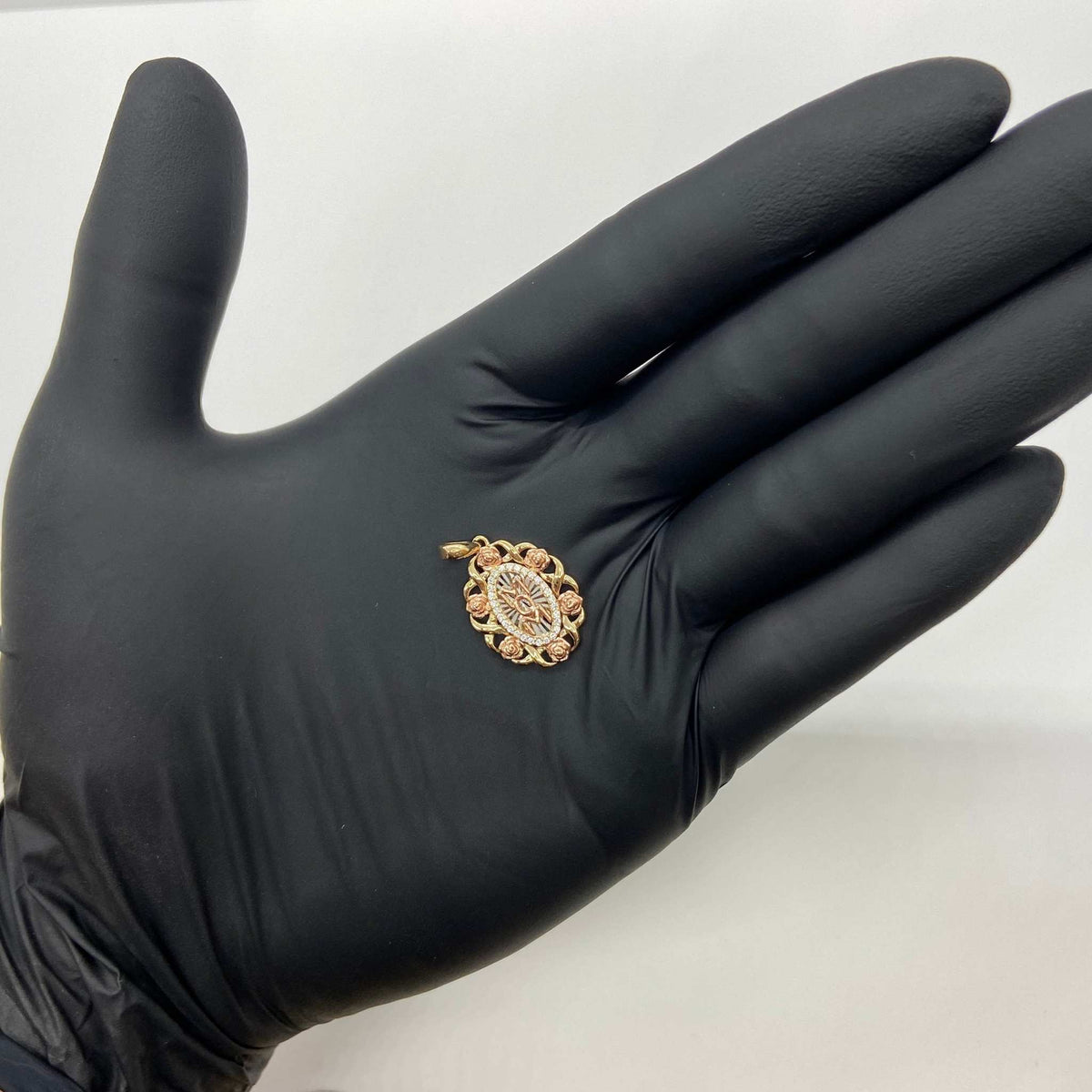Gloved hand holding a tri-color gold oval 'MOM' rose pendant charm.