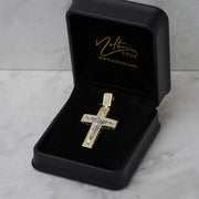 Gold and CZ square crucifix pendant inside an open black Nolters jewelry box with gold logo branding.