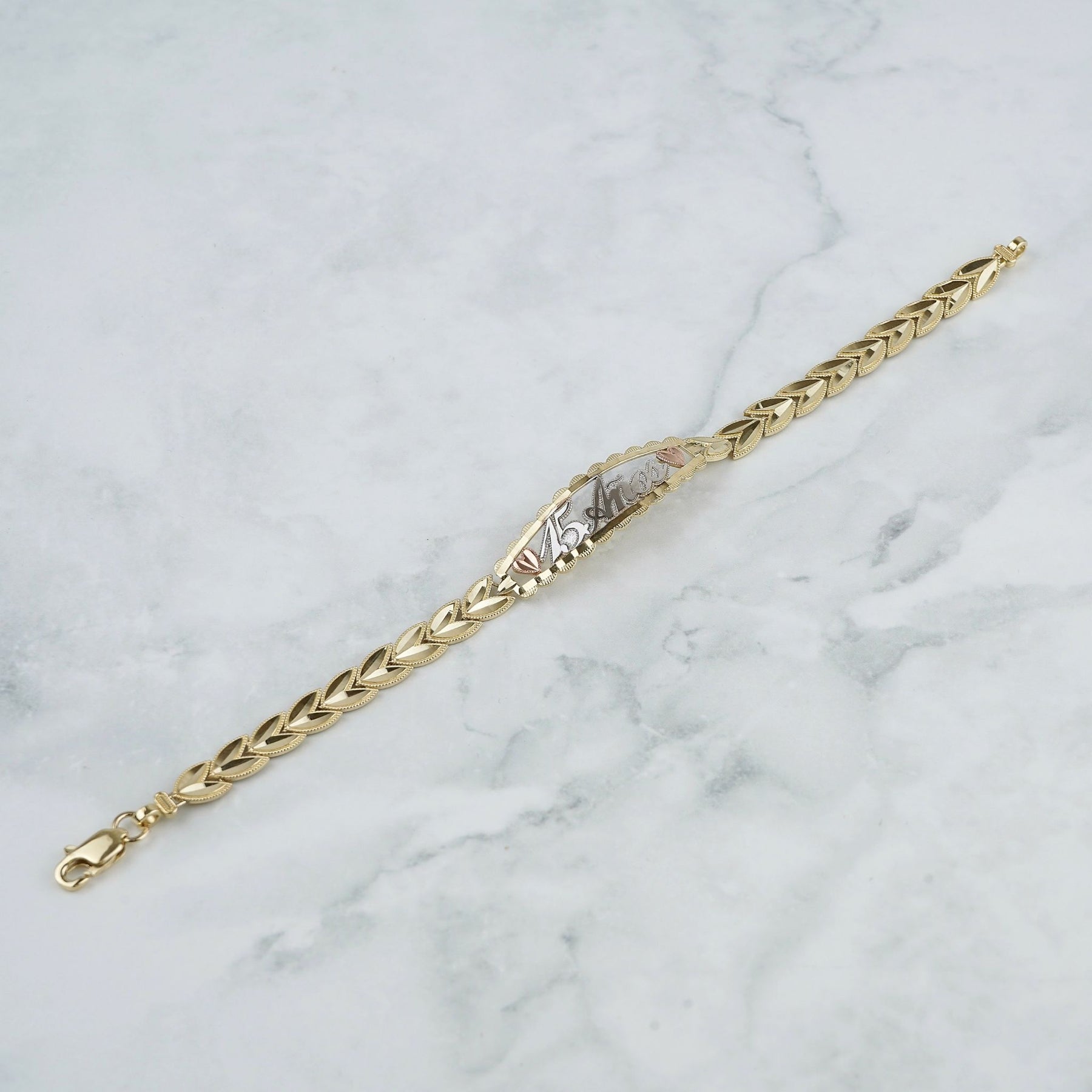 Tricolor gold Quinceañera leaf bracelet displayed diagonally on a white marble surface.