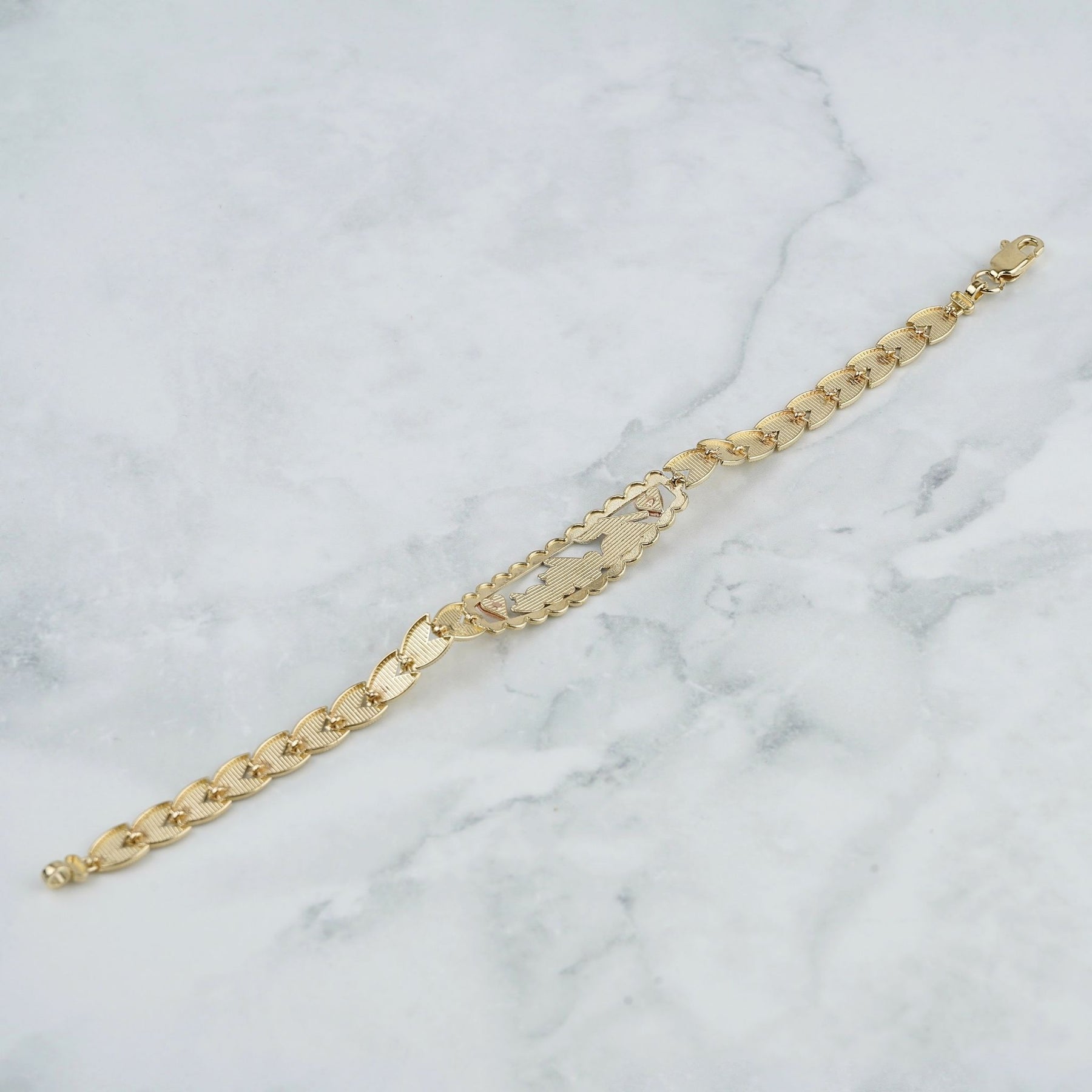 Back view of the tricolor gold Quinceañera leaf bracelet lying on a marble surface.