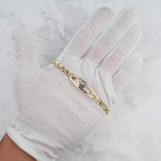 Tri-color gold quinceañera leaf bracelet displayed on a white-gloved hand against a marble surface.