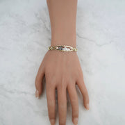 Tri-color gold quinceañera leaf bracelet displayed on a mannequin hand against a marble background.