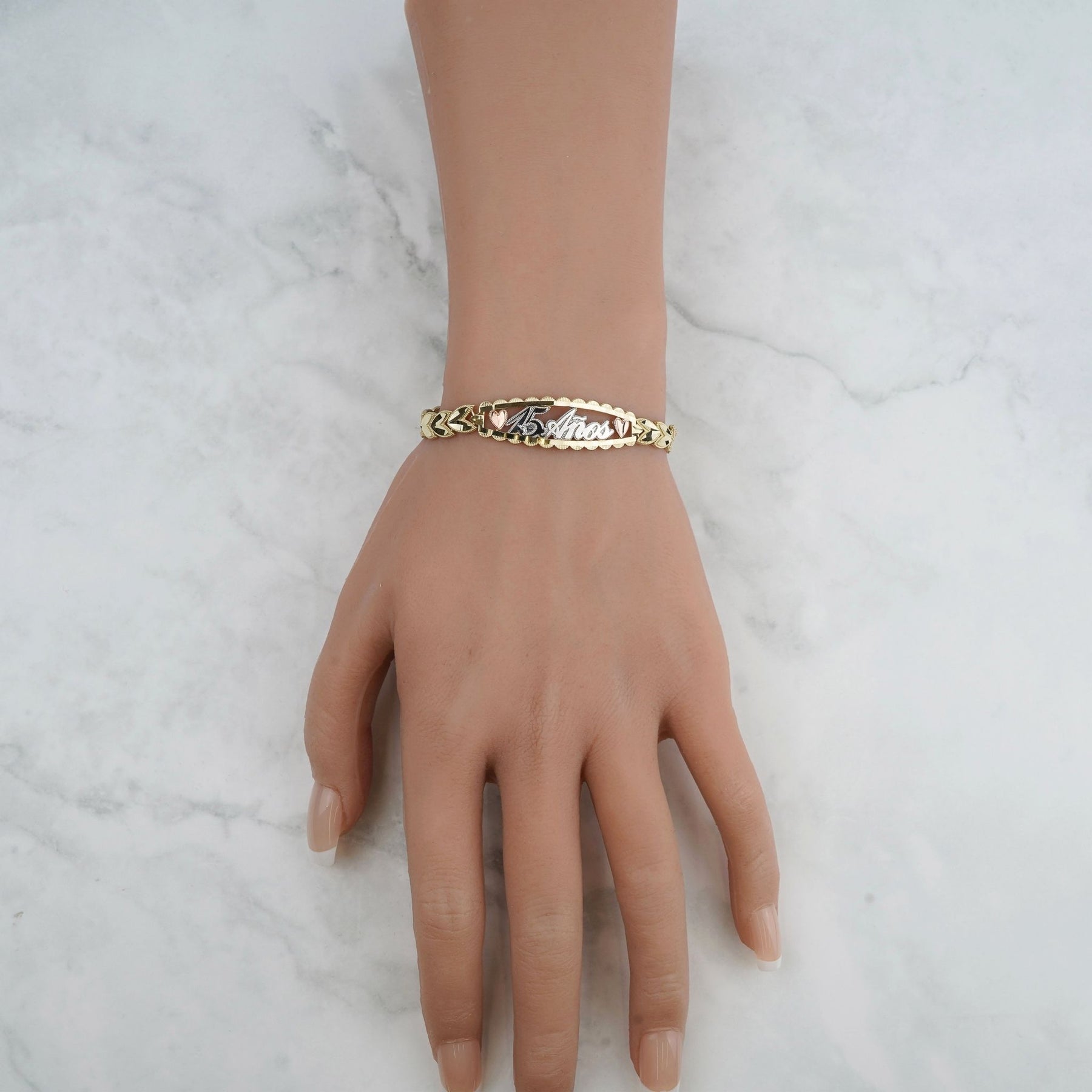 Tri-color gold quinceañera leaf bracelet displayed on a mannequin hand against a marble background.